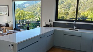 A modern kitchen with a large island, a built-in sink, and a view of lush greenery.