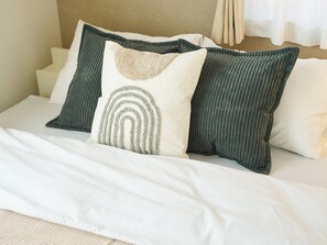 Un letto con biancheria bianca e tre cuscini, uno con motivo decorativo.