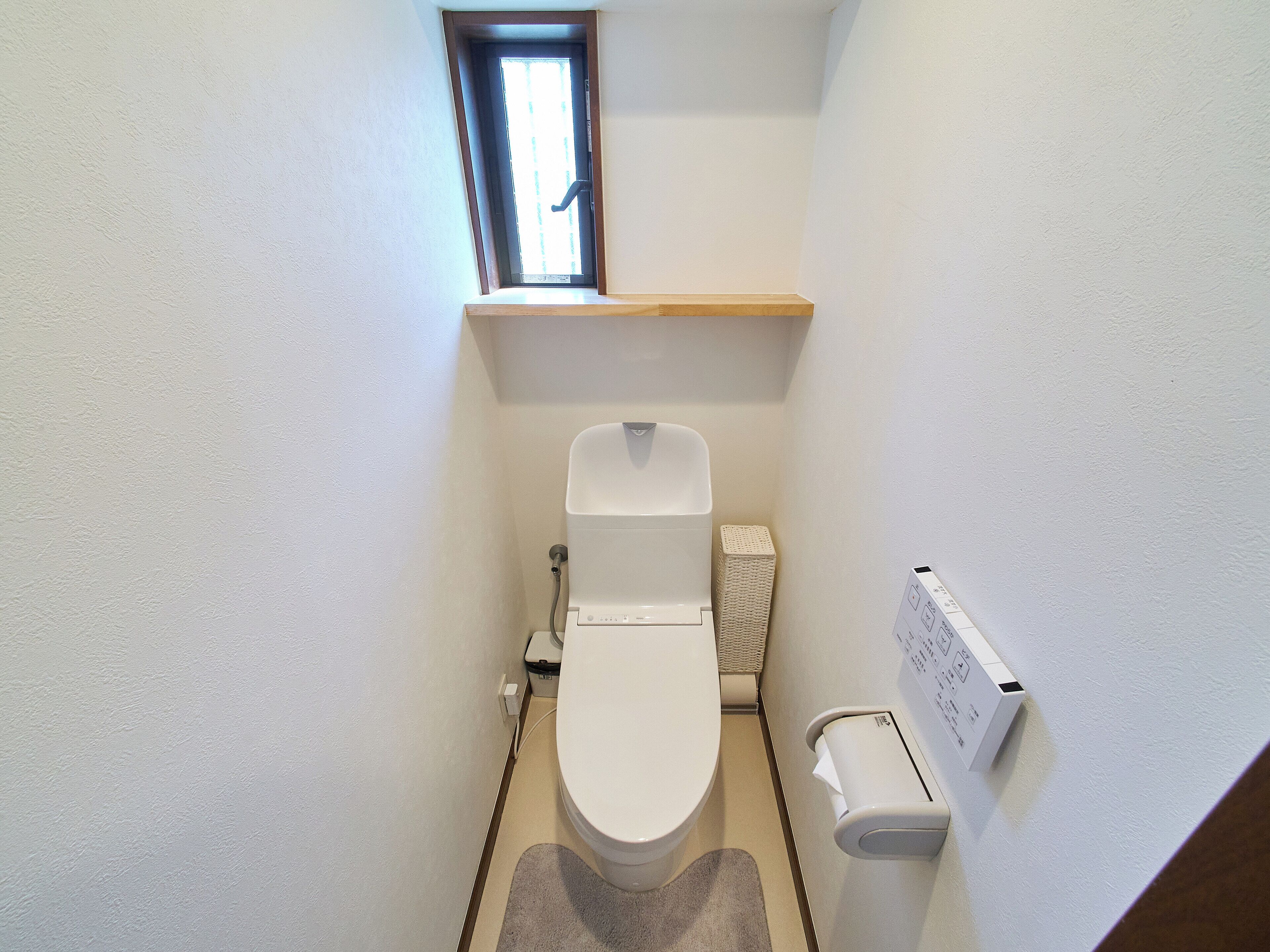Ein kleines, kompaktes Badezimmer mit Toilette, Handtrockner, Mülleimer und einem Fenster über der Toilette.