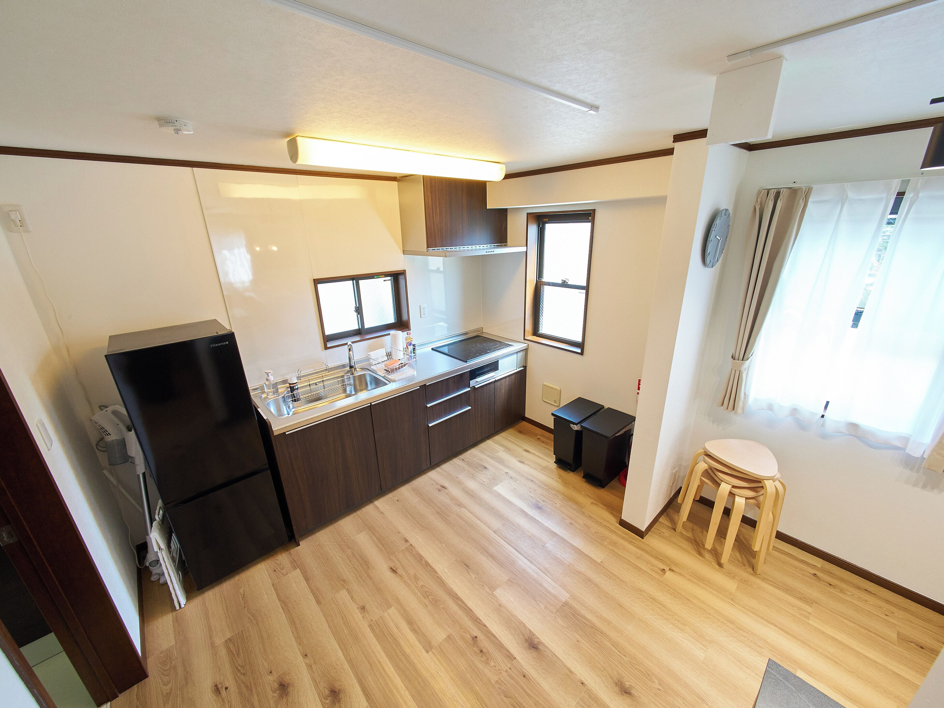 A compact kitchen with a refrigerator, sink, and stove, wooden flooring, and a window providing natural light.