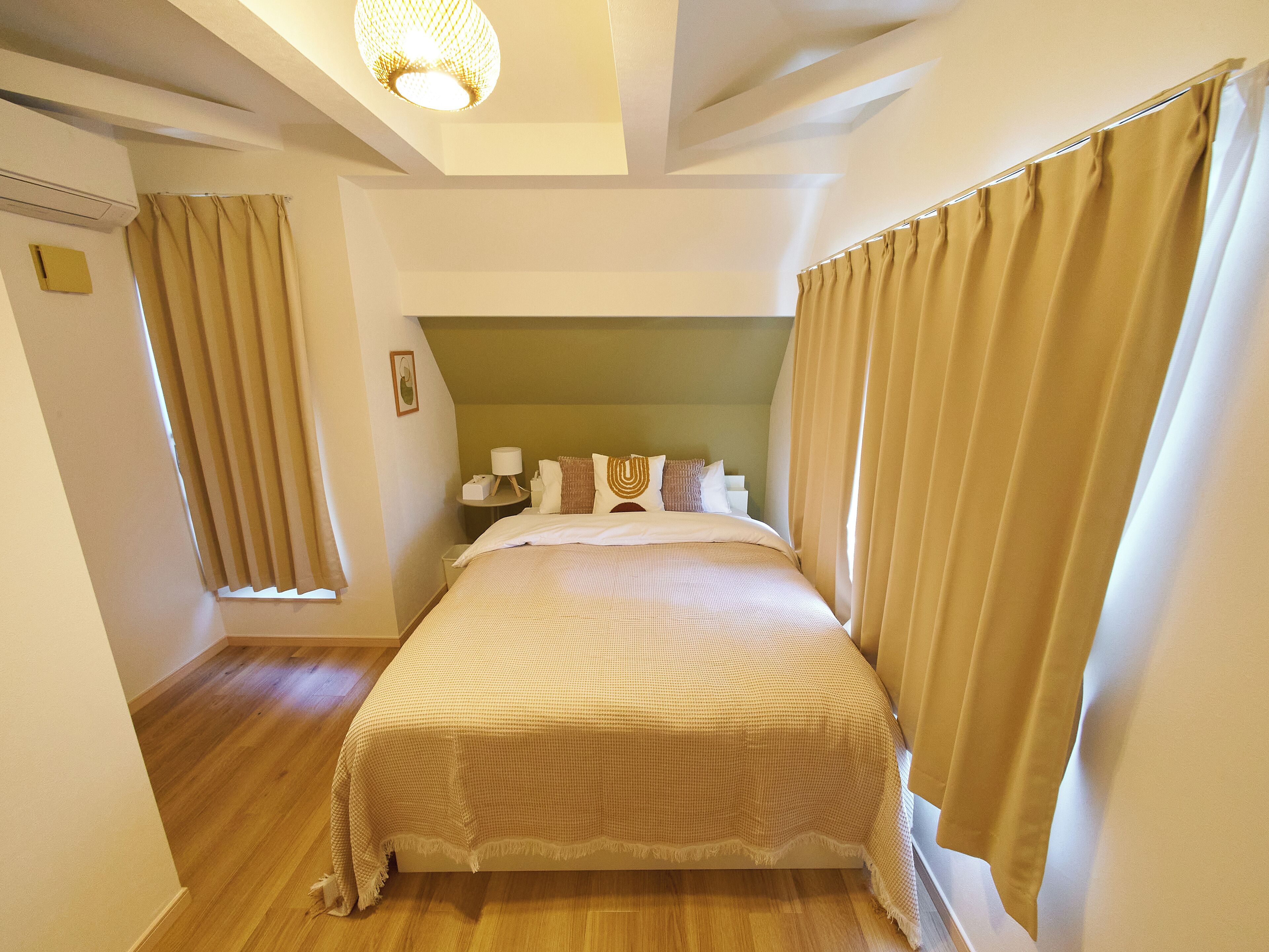 A hotel room with a large bed, beige curtains, a headboard, a bedside table with a lamp, and a small picture on the wall.