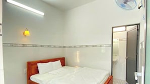 Una habitación limpia y bien iluminada con una cama de madera, un tapete pequeño y un ventilador de pared.