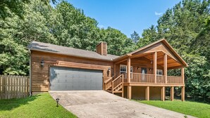 A wooden cabin with a garage, a covered porch, and a staircase leading to the entrance. - Trailhead Hideaway - bike & breathe! (Bella Vista)