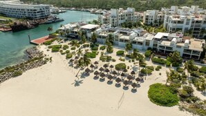 An aerial view of a coastal hotel with multiple buildings, a sandy beach, and palm trees. - Exclusive Condo | 3BR | Beachfront & Top Amenities (Cancún)