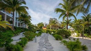 A pathway lined with palm trees and tropical plants leading to a building with balconies. - Exclusive Condo | 3BR | Beachfront & Top Amenities (Cancún)