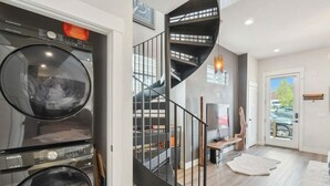 A modern interior with a spiral staircase, a washing machine, and a view through a glass door. - Chic Urban Loft Near Denver w/ Mtn Views (Westminster)