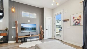 A modern living room with a large flat-screen TV, a wooden bench, and a large window. - Chic Urban Loft Near Denver w/ Mtn Views (Westminster)