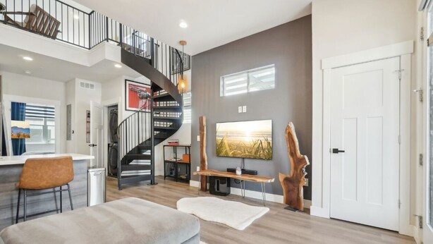 A modern living room with a spiral staircase, a large TV, and a rustic wooden sculpture. - Chic Urban Loft Near Denver w/ Mtn Views (Westminster)