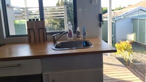 A modern kitchen with a wooden countertop, a stainless steel sink, and a window overlooking a backyard. - Relax in a Garden Retreat: Steps to Beaches,Shops,Stations and sdyney CBD. (Miranda)