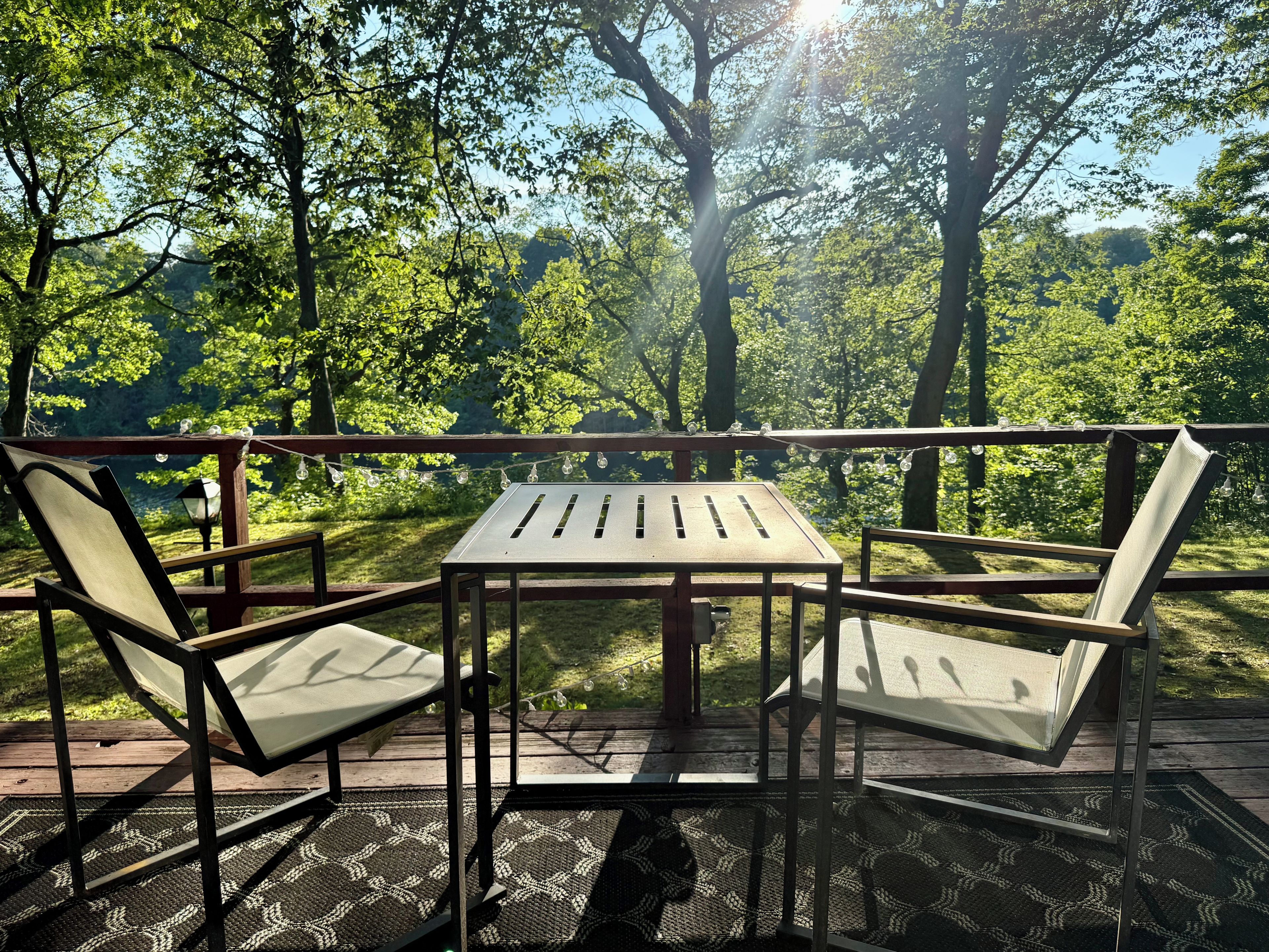 An outdoor deck with a table and two chairs, surrounded by trees and a view of the forest.