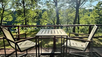 An outdoor deck with a table and two chairs, surrounded by trees and a view of the forest.