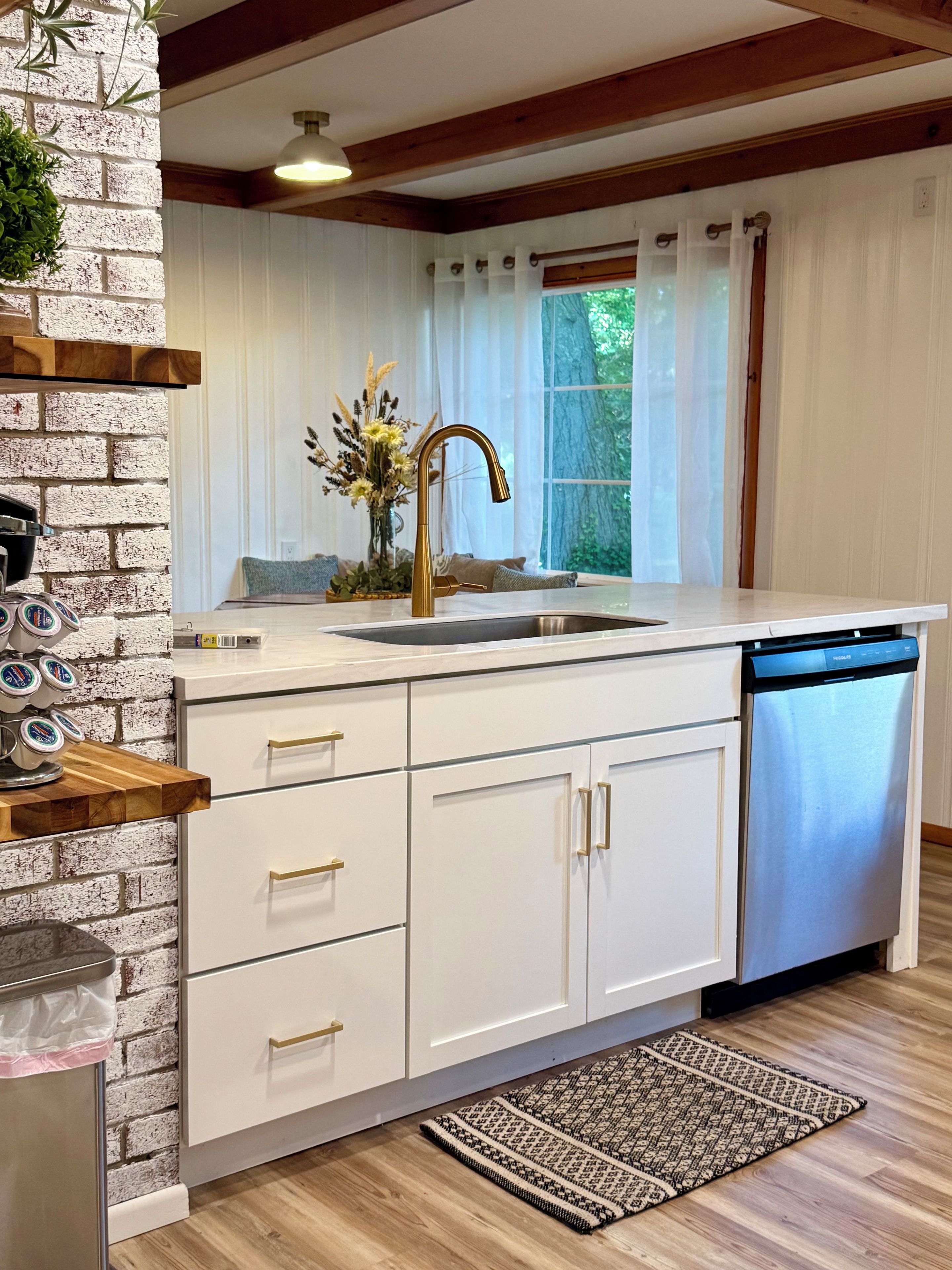 A modern kitchen with a white countertop, a gold faucet, and a dishwasher.