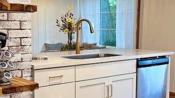 A modern kitchen with a white countertop, a gold faucet, and a dishwasher.