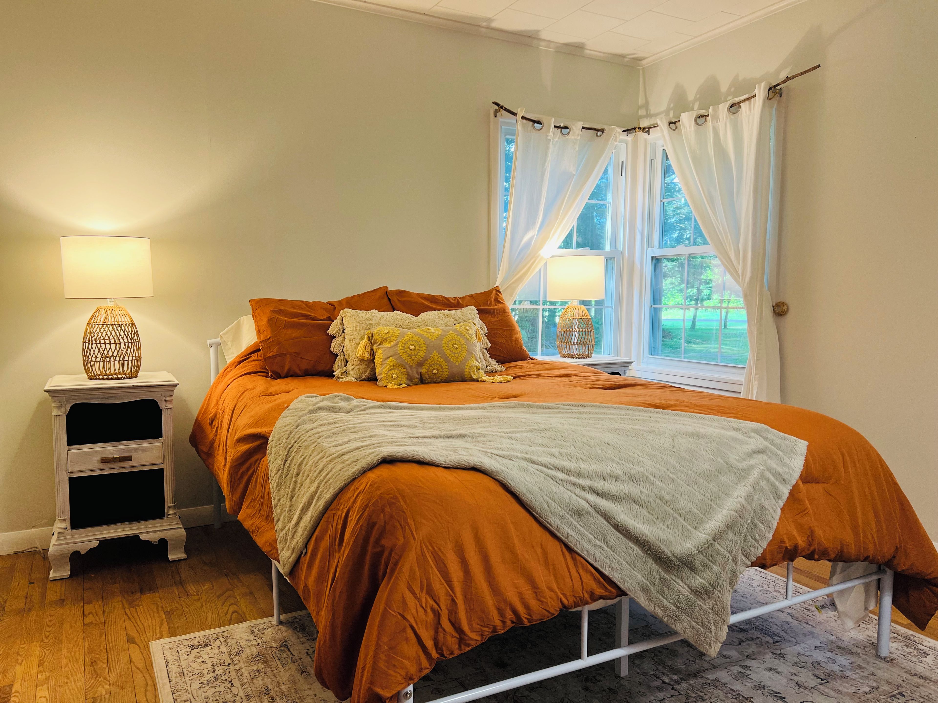 A bedroom with a bed, a nightstand, a lamp, and a window with curtains.