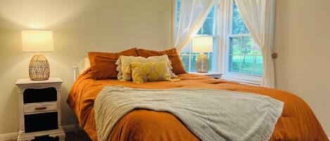 A bedroom with a bed, a nightstand, a lamp, and a window with curtains.