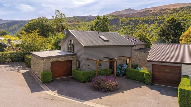 Ein Haus mit Garage, überdachter Terrasse und Blick auf einen bewaldeten Hang.
