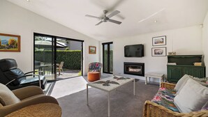 Ein modernes Wohnzimmer mit Deckenventilator, Kamin, Fernseher und großem Fenster.