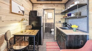 Une cuisine compacte aux murs en bois, un coin repas avec une table et des chaises, un réfrigérateur et un évier agrémenté d’un vase de fleurs.