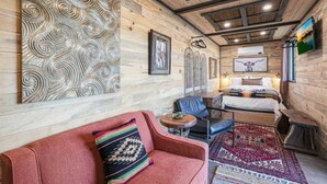 Une pièce chaleureuse avec un plafond en bois, un lit recouvert d’une courtepointe à motifs, un canapé rouge agrémenté d’un coussin coloré et une petite table ronde.