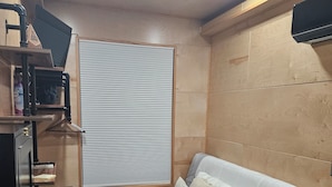 A compact bedroom with a bed, a wooden wardrobe, a small table, and a window with blinds. - Tiny Home Retreat with hot tub (Lake Villa)