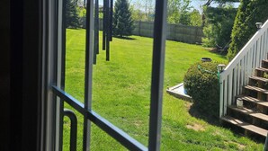 A view through a window with a metal grid, a grassy yard, a wooden staircase, and a tree. - Tiny Home Retreat with hot tub (Lake Villa)