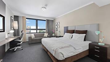 Une chambre d’hôtel avec un grand lit, un bureau, une chaise, un canapé et une table de chevet avec une lampe.