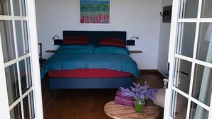 Quarto com cama, um quadro na parede e uma pequena mesa com flores.