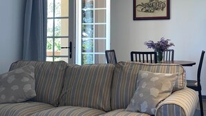 Sala de estar com sofá listrado, mesa de jantar, cadeiras e uma porta que dá para o exterior.
