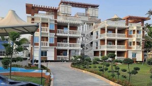 Un hôtel à plusieurs étages doté de balcons, d’une promenade dallée et de jardins aménagés.