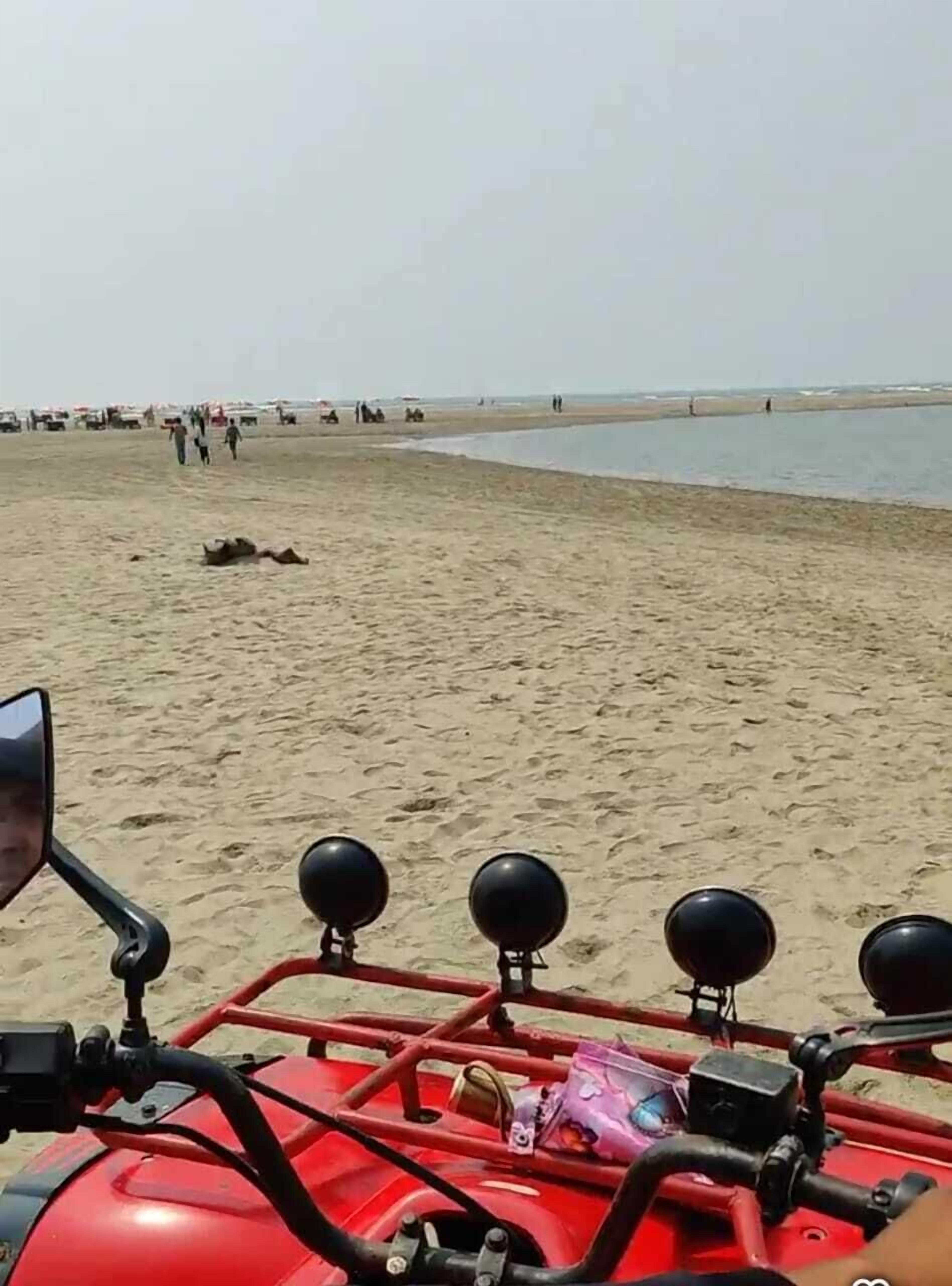 Una playa con un vehículo rojo en primer plano.
