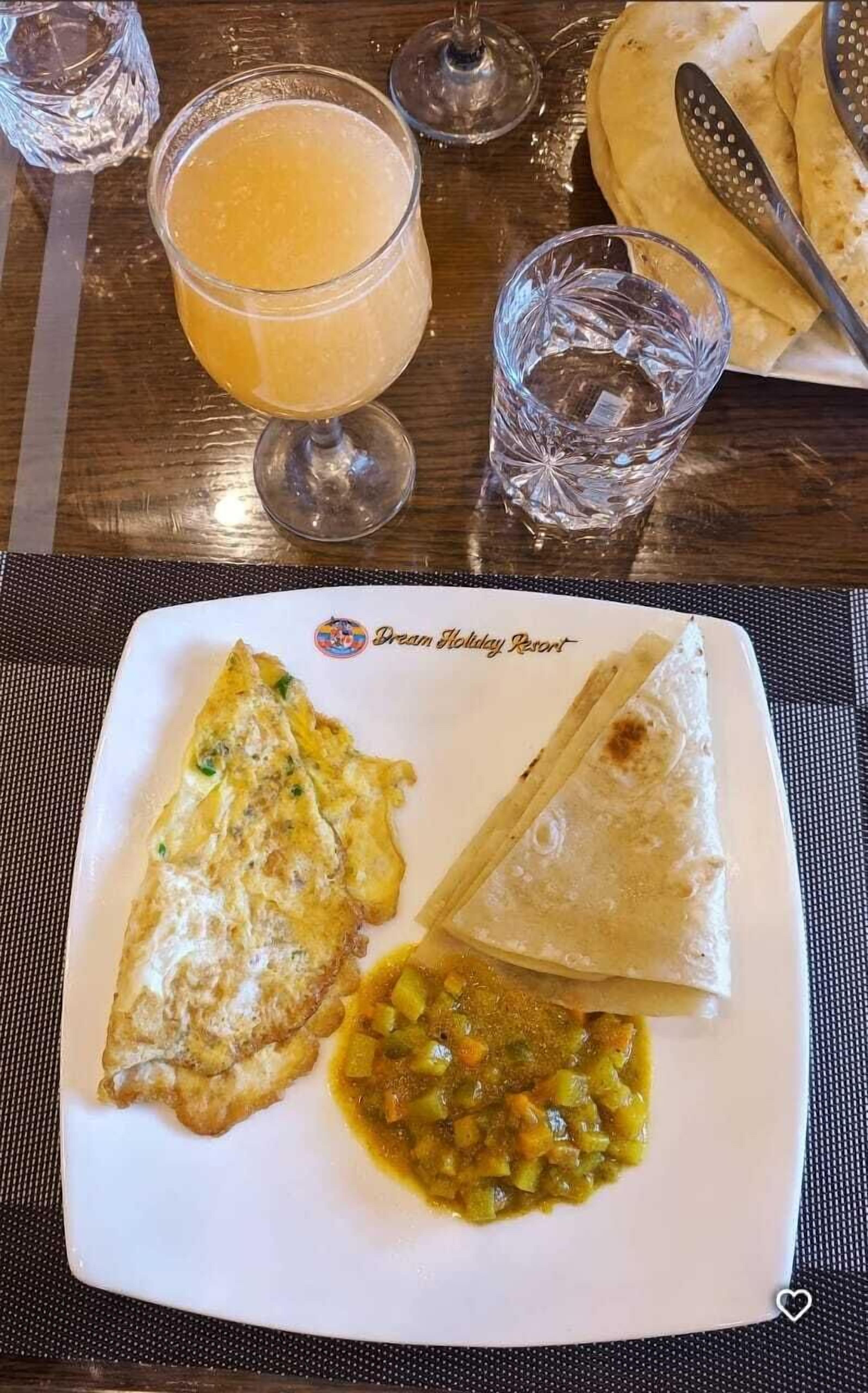 A plate with an omelette, two tortillas, and a vegetable dish, accompanied by a glass of orange juice and a water glass.