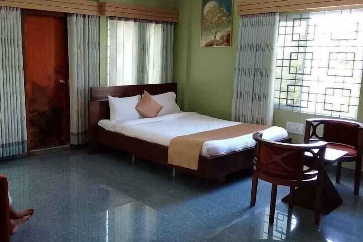 A hotel room with a bed, a chair, a table, and a painting on the wall.