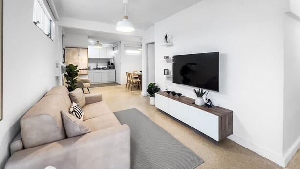 A modern living room with a beige sofa, a flat-screen TV mounted on a white wall, and a minimalist design. - Centric Modern Boho Apt For 6 @ San Juan (San Juan)