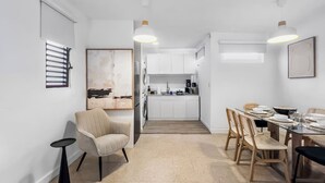 A modern kitchen with white cabinets, a dining area with a table set for four, and a chair. - Centric Modern Boho Apt For 6 @ San Juan (San Juan)