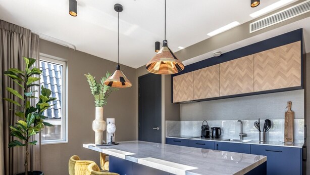 A modern kitchen with a central island, bar stools, pendant lighting, and a potted plant. - Apartment, Near the Beach and the sea (The Hague)