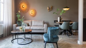 A modern living room with a sofa, two armchairs, a coffee table, and a dining area with a table and chairs. - Apartment, Near the Beach and the sea (The Hague)