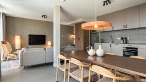 A modern kitchen with a dining area, featuring a wooden table, chairs, and a hanging light fixture. - Apartment, Near the Beach and the sea (The Hague)