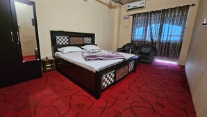 A bedroom with a bed, a chair, a wardrobe, and a window with curtains. - Hotel Anshdeep Palace (Jogindarnagar)