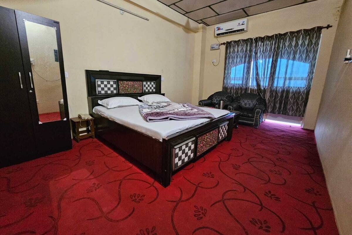 A bedroom with a bed, a chair, a wardrobe, and a window with curtains.