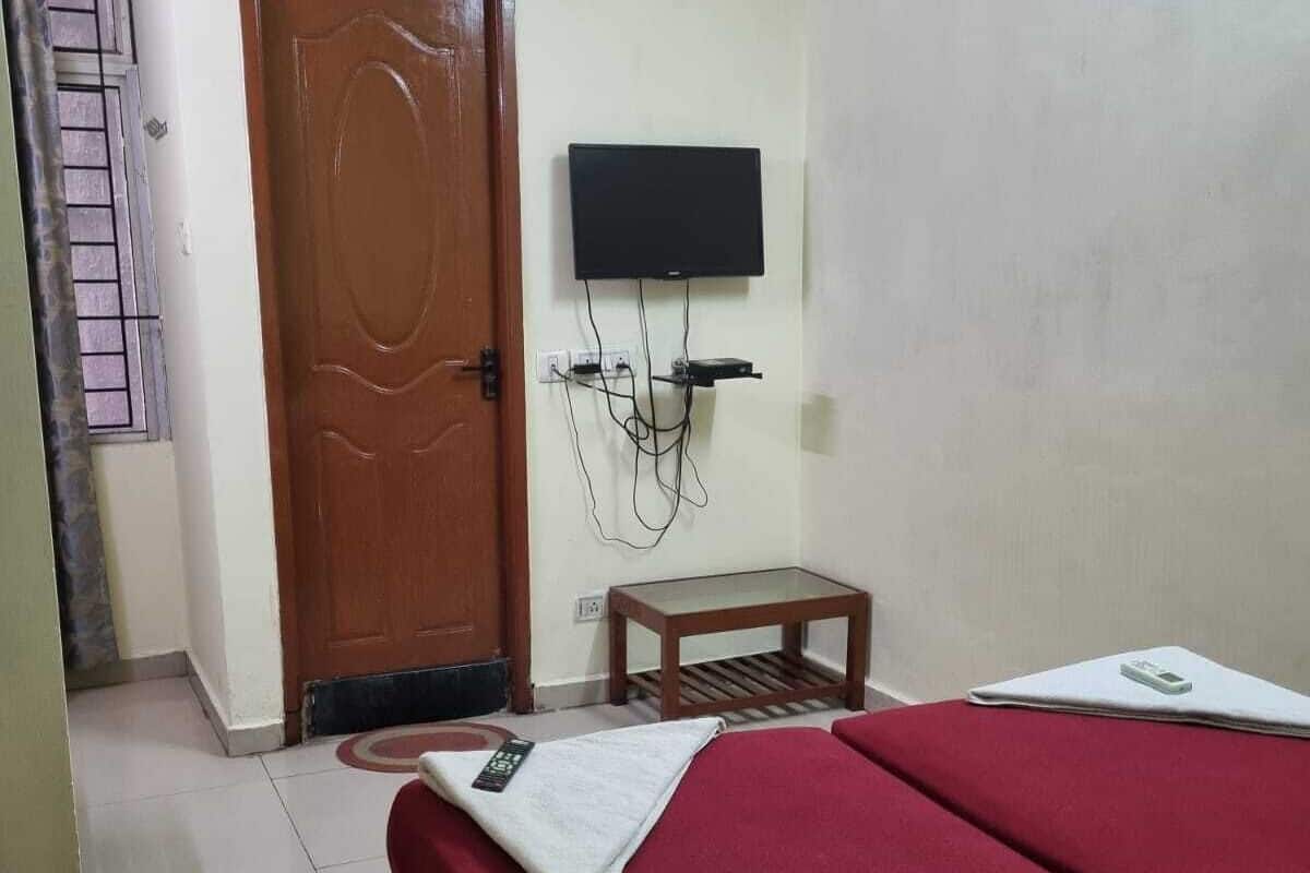 A hotel room with a bed, a TV mounted on the wall, an air conditioning unit above the door, and a small table.
