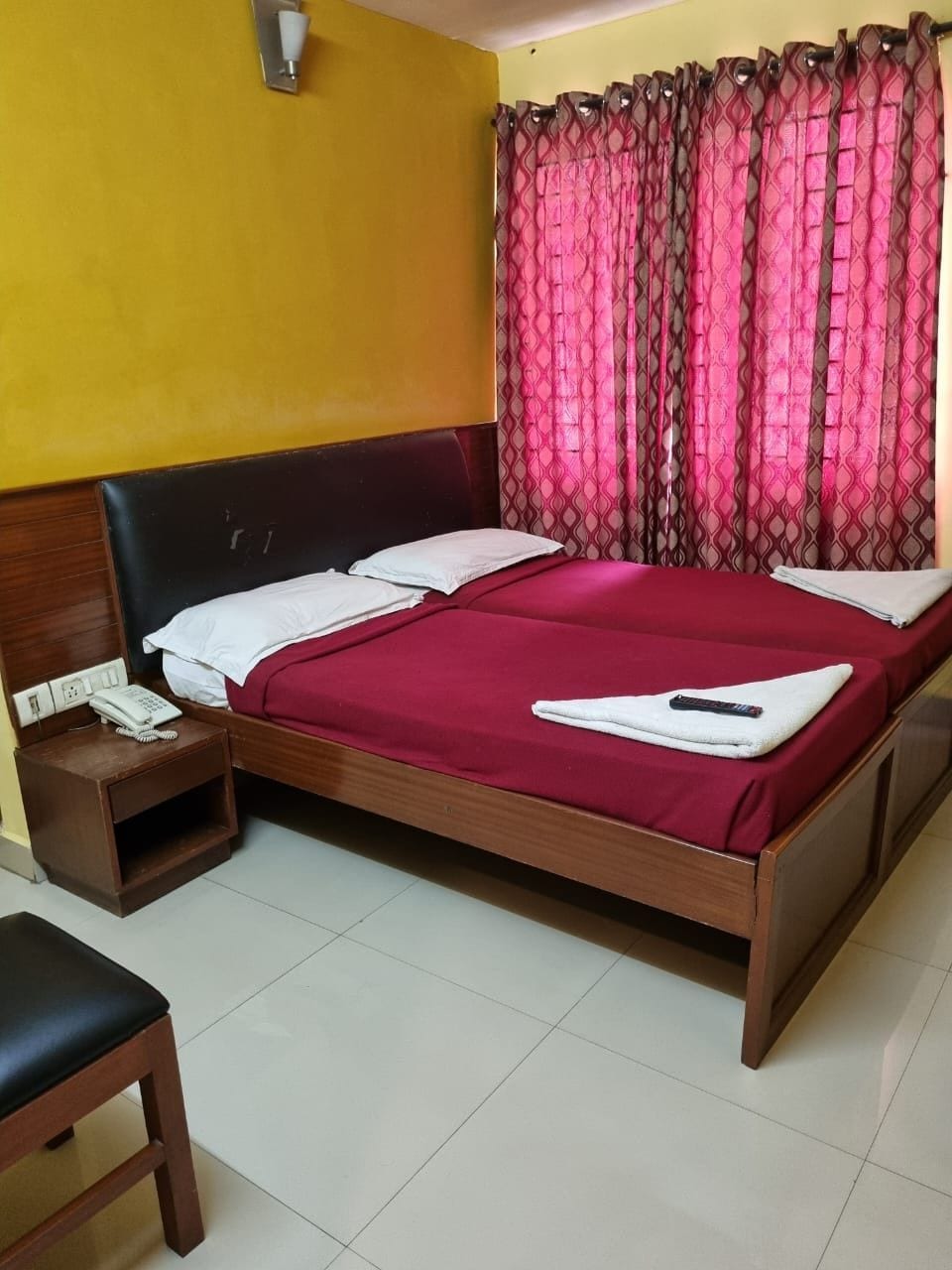 A single bed with a wooden headboard, a bedside table with a phone, and a chair.