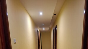 A hallway with yellow walls, wooden doors, and a tiled floor. There are two trash bins and a ceiling light fixture. - SEA SHELL PARK  (Chennai)
