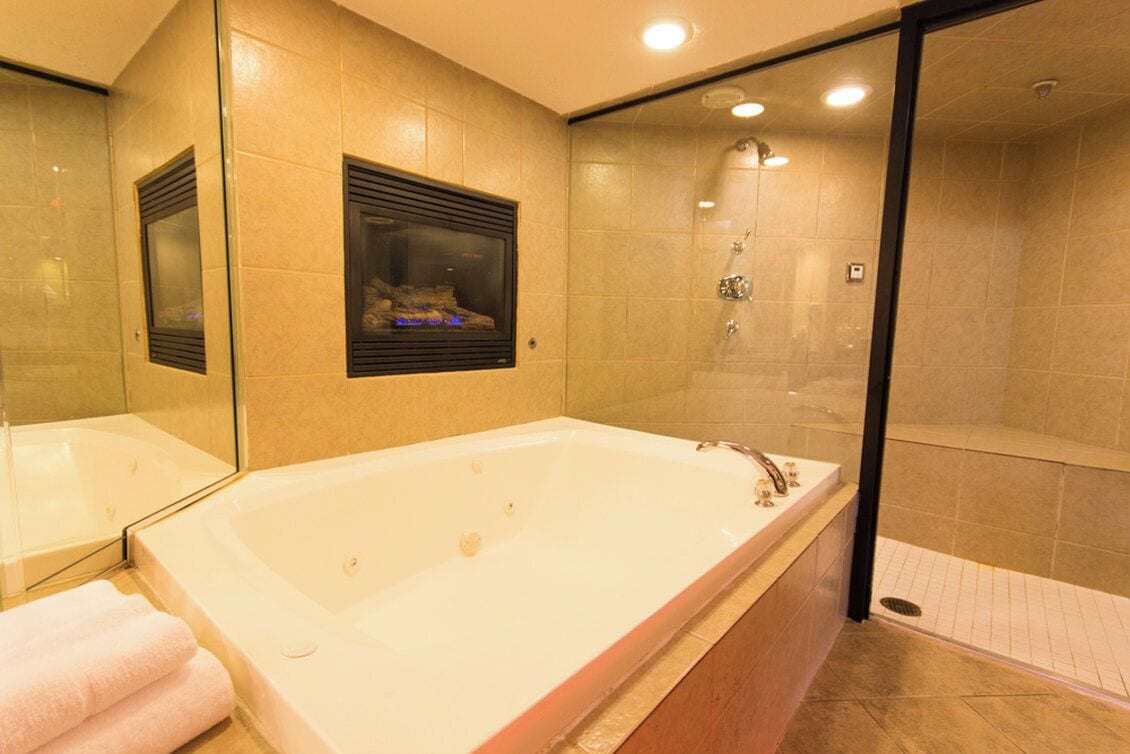 Un baño moderno con una bañera grande, un box de ducha de vidrio y un espejo con estante integrado.