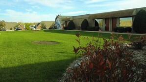 A building with a flat roof, large windows, and a well-maintained lawn with a circular flower bed. - Essence Suites (Orland Park)