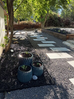 A garden pathway with stepping stones, potted plants, and a wooden fence.