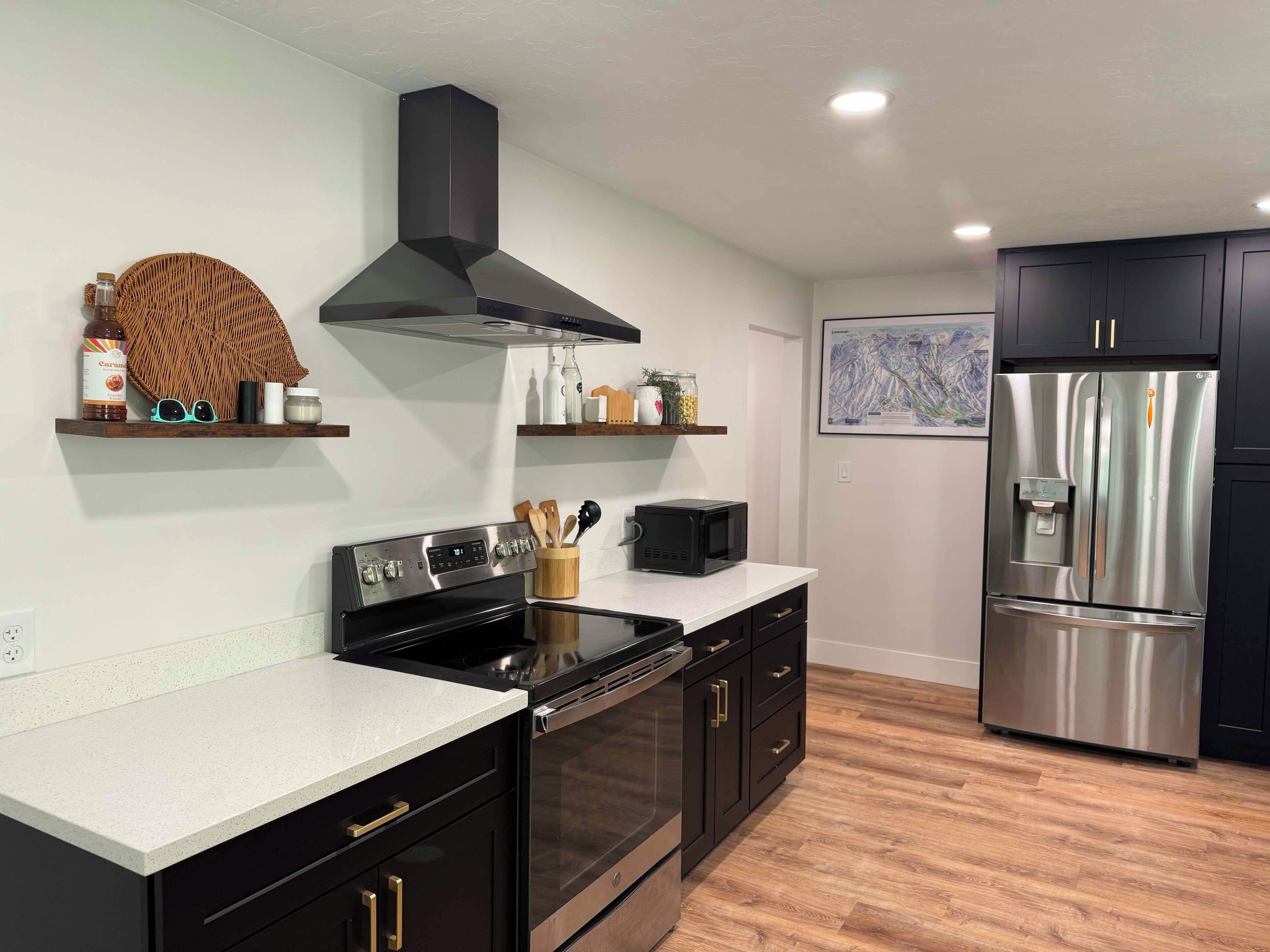 Une cuisine moderne avec des meubles de couleur sombre, des appareils électroménagers en acier inoxydable et un plancher en bois.