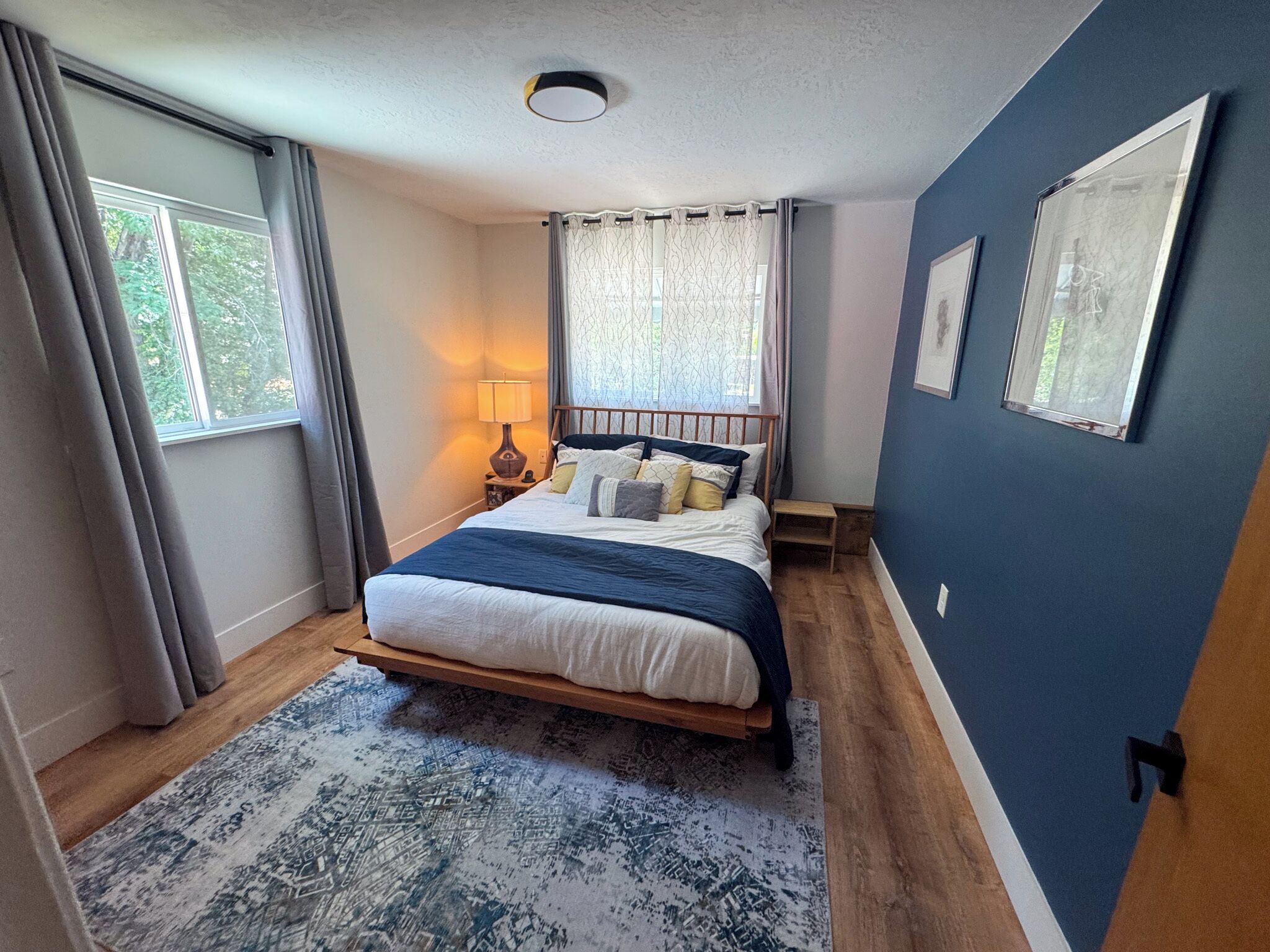 A bedroom with a bed, a nightstand, a lamp, a window with curtains, and a blue wall.
