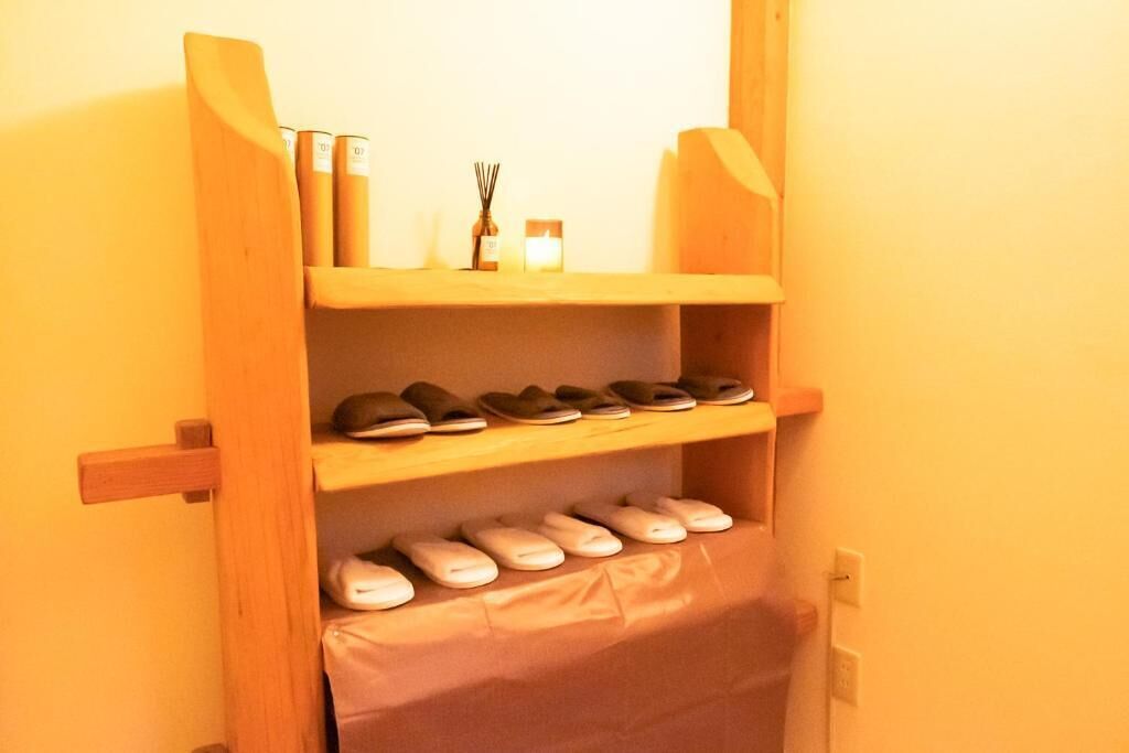 A wooden shoe rack with multiple shelves holding shoes and a small shelf with candles and a diffuser.