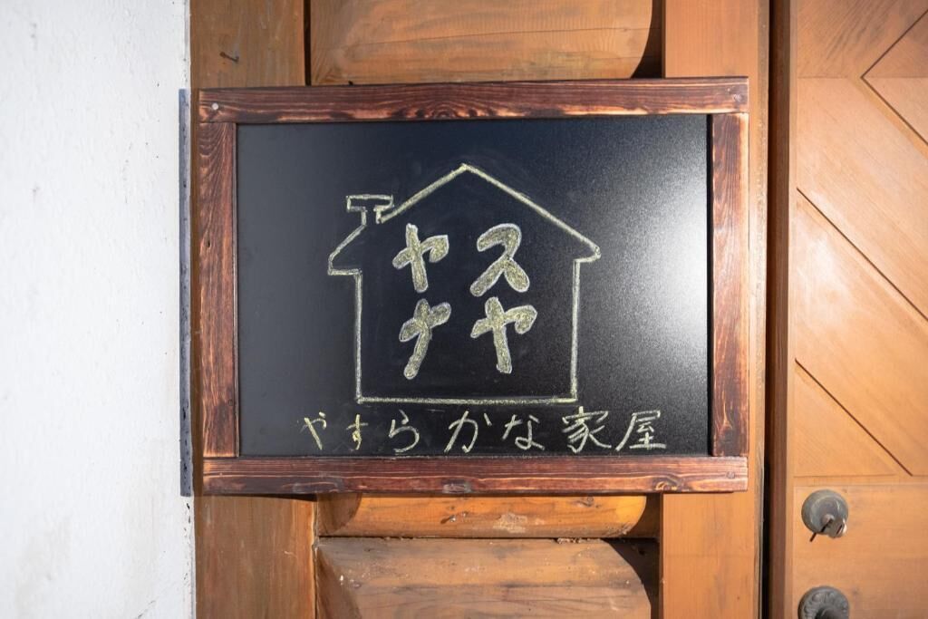 A blackboard with a house outline and Japanese text, likely indicating a hotel name or type.