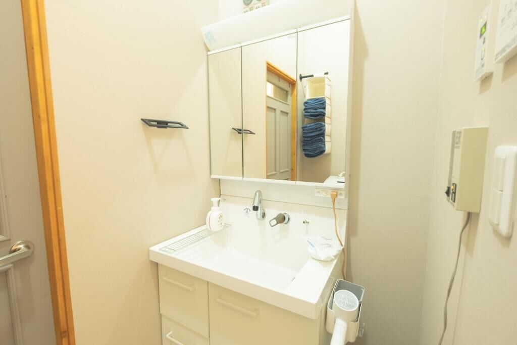 Un baño con un lavamanos blanco, un espejo, un perchero y un secador de manos.